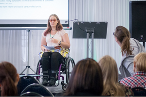 A woman in a wheelchair delivering a presentation and the heads of people in the audience