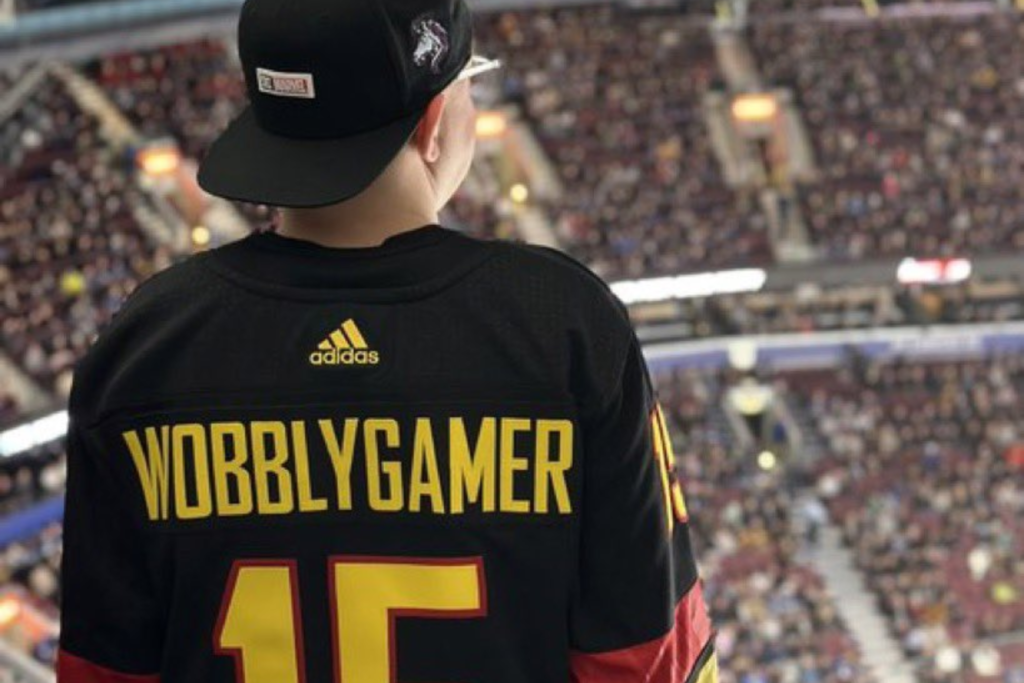 Matt Allcock aka the Wobbly Gamer is facing away from the camers looking out onto a stadium. The back of his personalised football shirt says 'WOBBLY GAMER'.