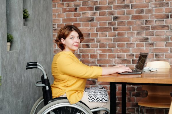 Woman in a wheelchair is working at a laptop, facing the camera.