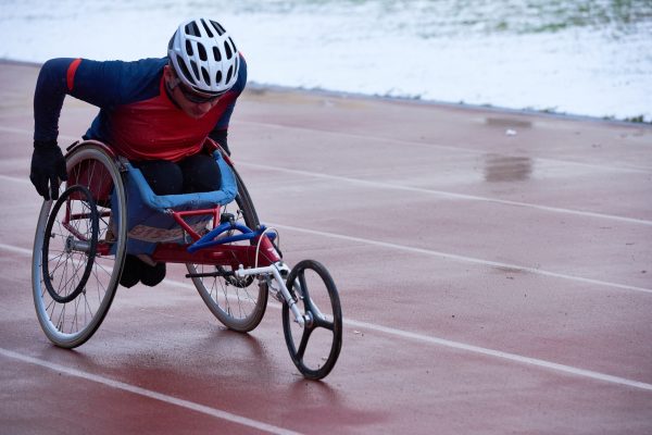Athlete in sportswear and helmet training in racing wheelchair at outdoor track and field stadium, to illustrate an article on disability in sports and e-sports media representation.